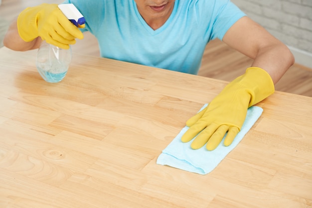 Onherkenbare man in rubberen handschoenen spuiten tafel en schoonmaken