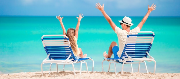 Panorama van familie van vader en kind handen omhoog op strand zittend op chaise-longue Premium Foto
