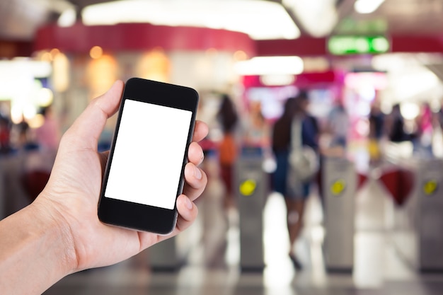 Persoon met behulp van smartphone witte scherm houder bij de hand met wazige achtergrond van mensen die langs ticket machines in elektrische treinstation lopen. Premium Foto