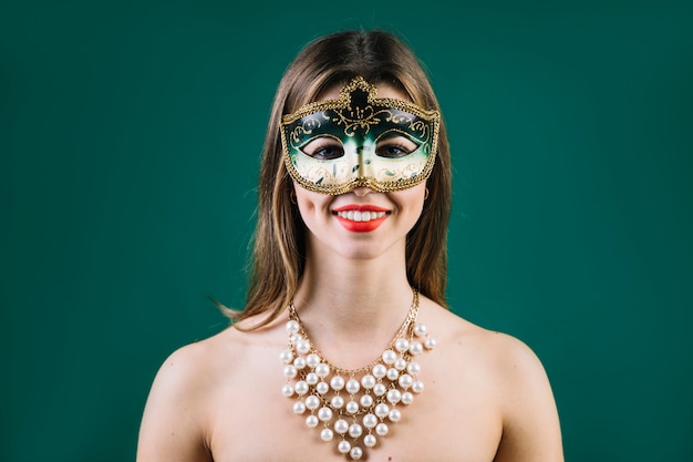 Portret van een glimlachende vrouw die carnaval-masker op gekleurde achtergrond draagt Gratis Foto