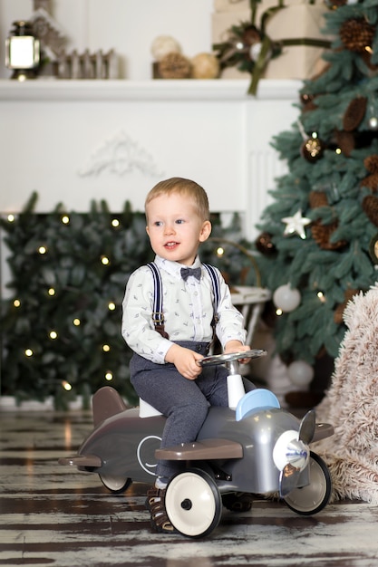 Portret van een kleine jongenszitting op een uitstekend stuk speelgoed vliegtuig dichtbij een kerstboom. kerst versiering. de jongen verheugt zich op zijn kerstcadeau. vrolijk kerstfeest en een gelukkig nieuwjaar Premium Foto