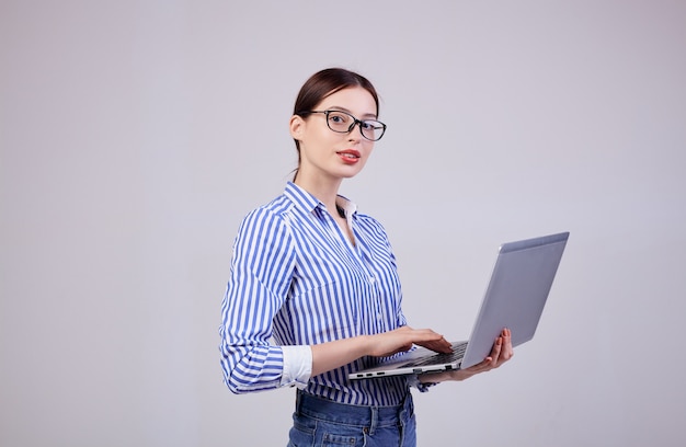 Portret van een vrouwelijke beheerder in een gestreept wit-blauw shirt met een bril en een laptop op grijs. werknemer van het jaar, zakelijke dame. kopieer ruimte. Premium Foto