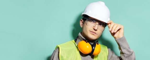 Portret van jonge ingenieur bouwvakker veiligheidshelm, bril, jas dragen op achtergrond van aqua kleur. | Premium Foto