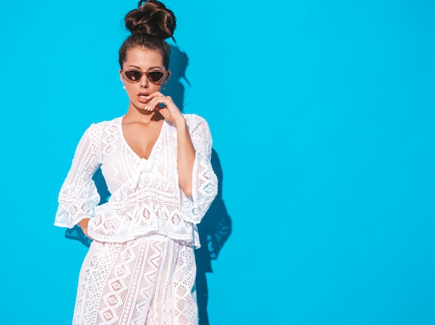 Portret van jonge mooie sexy vrouw met lijkenetende kapsel. trendy meisje in casual zomer witte hipster pak kleding in zonnebril. heet model dat op blauw wordt geïsoleerd Gratis Foto