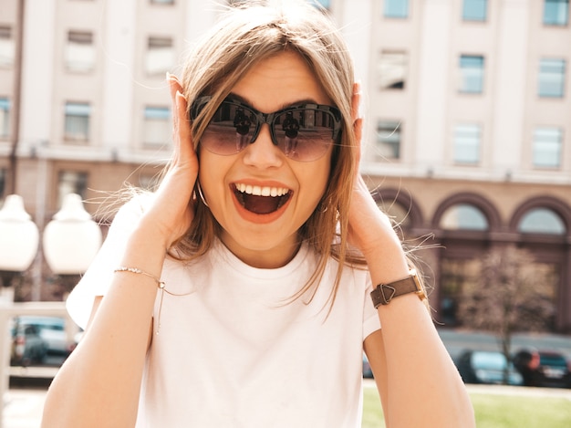 Portret van mooi verrast blond model gekleed in de zomer hipster kleren. het trendy meisje stellen op de straatachtergrond. grappige en geschokte vrouw Gratis Foto