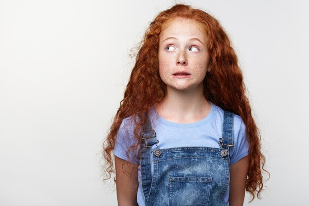 Portret schuldig schattig klein meisje met rood haar, beweert niets verkeerd te doen, kijkt weg over witte achtergrond met kopie ruimte aan de linkerkant. | Gratis Foto