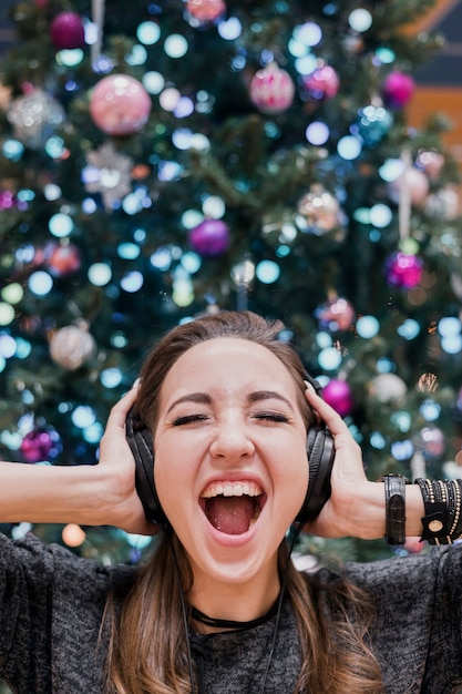 Portret van vrouw met hoofdtelefoons en het schreeuwen dichtbij kerstmisboom Gratis Foto