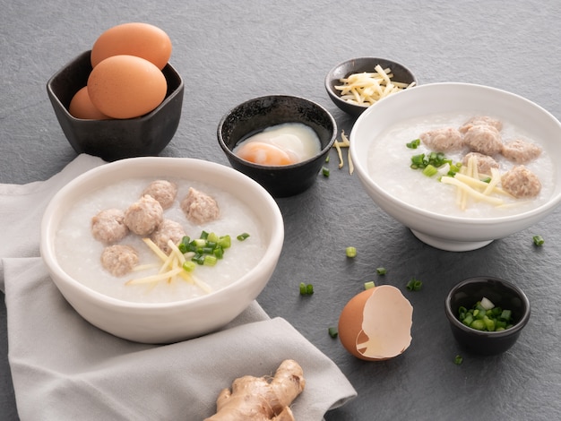 Rijstcongee met fijngehakt varkensvlees in witte kom. kom rijstepap met zacht gekookt ei. aziatisch ontbijt Premium Foto