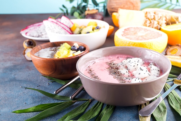 Rode of roze die smoothieaai kommen met verse pitaya en chiazaden worden bedekt op palmblad op steenachtergrond, exemplaarruimte Premium Foto