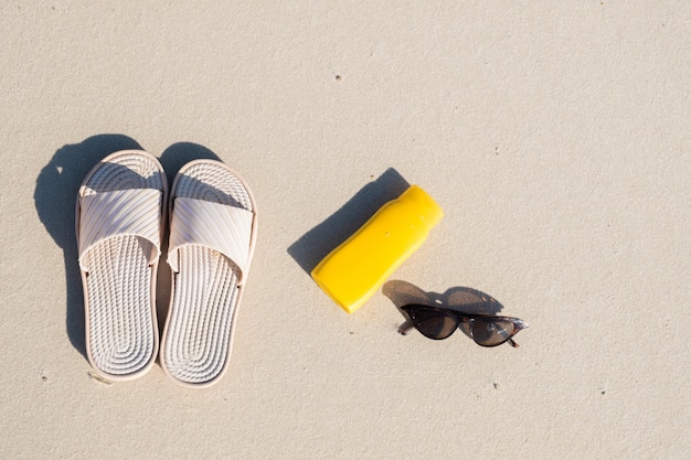 Rust op het strand: slippers, beschermende crème en zonnebril op schoon zand. bovenaanzicht van accessoires voor vakanties aan zee of zomervakantie Premium Foto