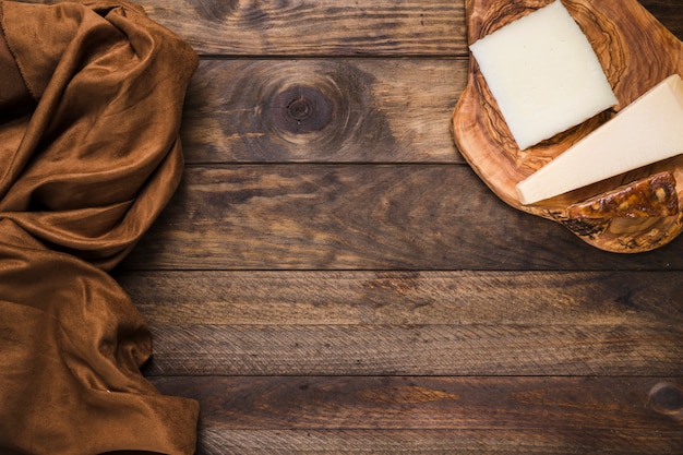 Smakelijke kaas op houten kaasplank met bruine zijdestof over oude houten oppervlakte Gratis Foto