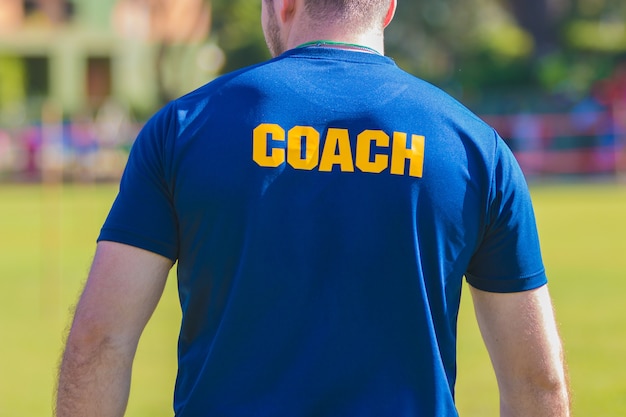 Sporttrainer In Blauw Shirt Met Gele Coach Tekst Op De Rug