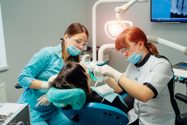 Stomatoloog en hulpvrouwen in maskers en beschermende glazen die met een vrouwelijke patiënt in tandartsbureau werken. Premium Foto
