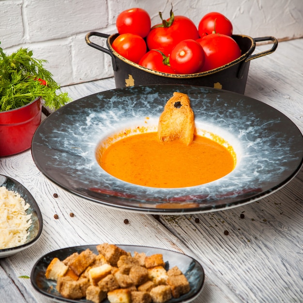 Tomatensoep met verse tomaten, groenen en kaas op tafel Gratis Foto