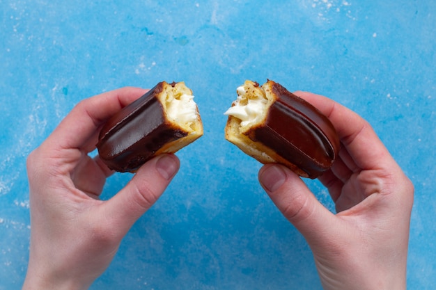 Traditioneel frans dessert. heerlijke eclair met vla en chocoladesuikerglazuur in tweeën in handen gekraakt. gebak, zoet voedsel voor zoetekauw Premium Foto