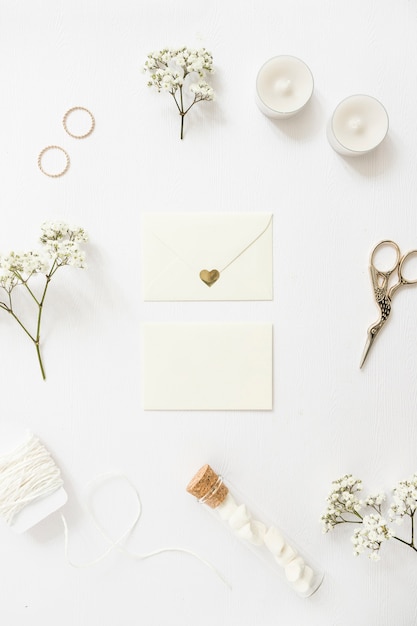 Twee enveloppen omringd met trouwringen; kaarsen; schaar; draad; reageerbuis en baby's-adem bloemen op witte achtergrond Gratis Foto
