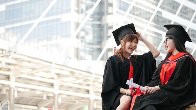 Twee meisjes in zwarte toga's en houden diploma-certificaat zitten en lachend met gelukkig afgestudeerd. Premium Foto
