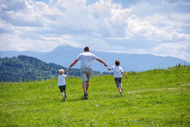 Vader en twee jonge zonen die op het groene veld hand in hand lopen Premium Foto