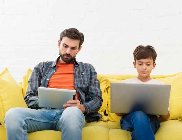 Vader op tablet kijken en zoon die aan laptop werken Gratis Foto