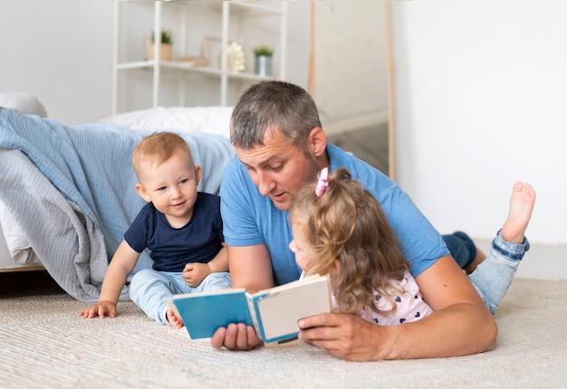 Vader zittend op de vloer en lezen voor kinderen Gratis Foto