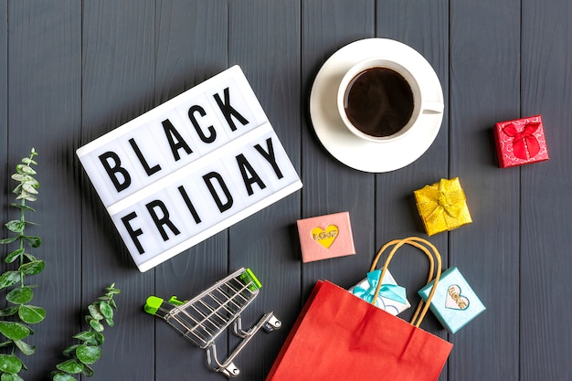 Veelkleurige verpakkingstassen, trolley, takje eucalyptus, kopje koffie geschenkdozen lightbox met tekst black friday op donkergrijs oppervlak Premium Foto