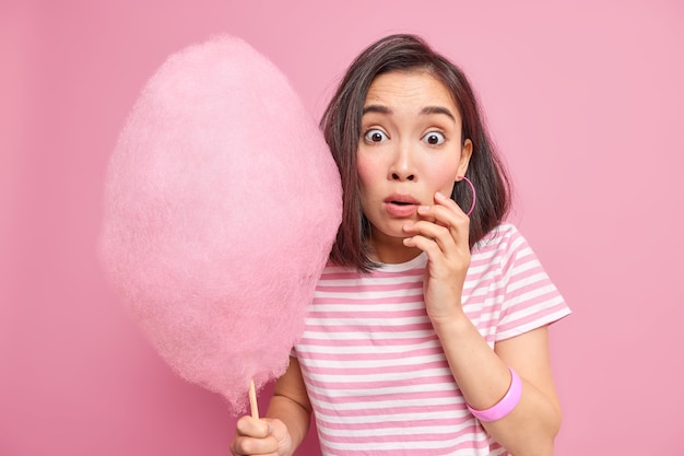 Defecte suiker architect Verbijsterd bang brunette vrouw houdt zoete suikerspin verrast om iets  geweldigs te horen ontdekt hoeveel calorieën ze gaat eten draagt gestreept  t-shirt geïsoleerd over roze muur. | Gratis Foto