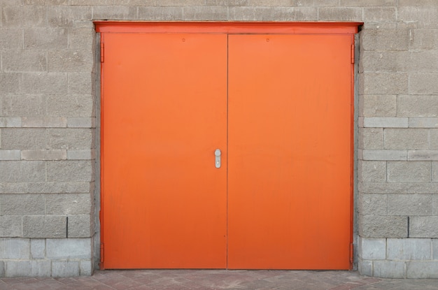 Vooraanzicht van brede oranje felrode deur in grijze stenen bakstenen muur met randen | Premium Foto