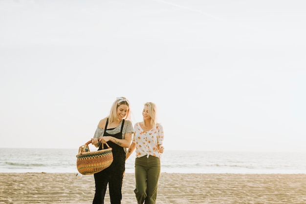 Vrienden die bij het strand met een picknickmand lopen Gratis Foto