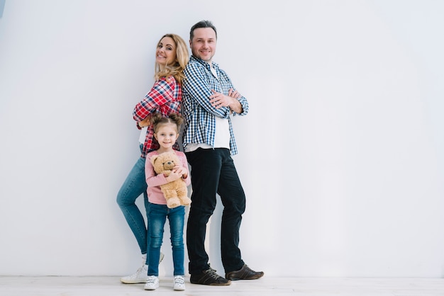 Vrolijk paar met hun dochter die vooraan witte muur stellen Gratis Foto
