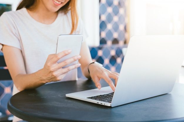 Vrolijke aziatische jonge vrouwenzitting in koffie het drinken koffie en het gebruiken van smartphone voor het spreken Gratis Foto