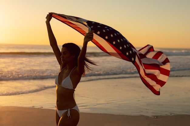 Uitgelezene Vrouw die zich met golvende amerikaanse vlag op het strand bevindt JO-07