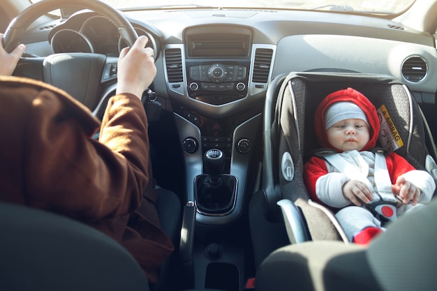 Vrouw rijdt in de auto, en haar kleine kind zit voorin, met een veiligheidsgordel. | Premium Foto