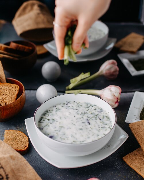 Yoghurt dovga met groenen binnen ronde witte plaat samen met brood