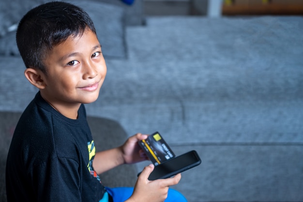Yong aziatische kinderen met gele huid, met zwarte creditcard, zwarte laptop op witte tafel. Premium Foto