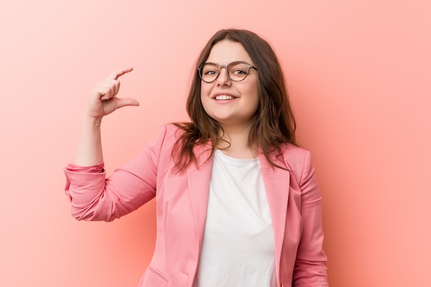 Young plus size zakelijke blanke vrouw met iets kleins met wijsvingers, glimlachend en zelfverzekerd. Premium Foto