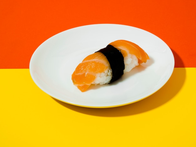Zalmsushi op een witte plaat op een gele en oranje achtergrond Gratis Foto