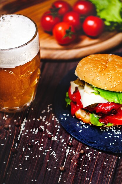 Zelfgemaakte watertanden, heerlijke rundvleesburger met sla en aardappel, glas bier geserveerd op stenen snijplank. donker Premium Foto