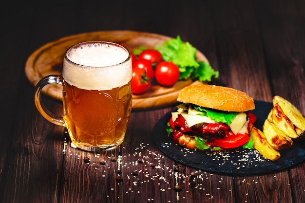Zelfgemaakte watertanden, heerlijke rundvleesburger met sla en aardappel, glas bier geserveerd op stenen snijplank. donker Premium Foto