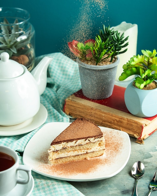 Zijaanzicht tiramisu dessert met een boek en een plant op tafel