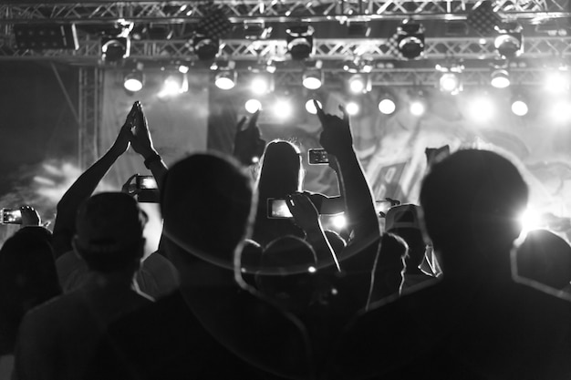 Zwart-wit silhouet van mensen in menigte op een muziekfestival. concert met verlichte staande dansende mensen Premium Foto